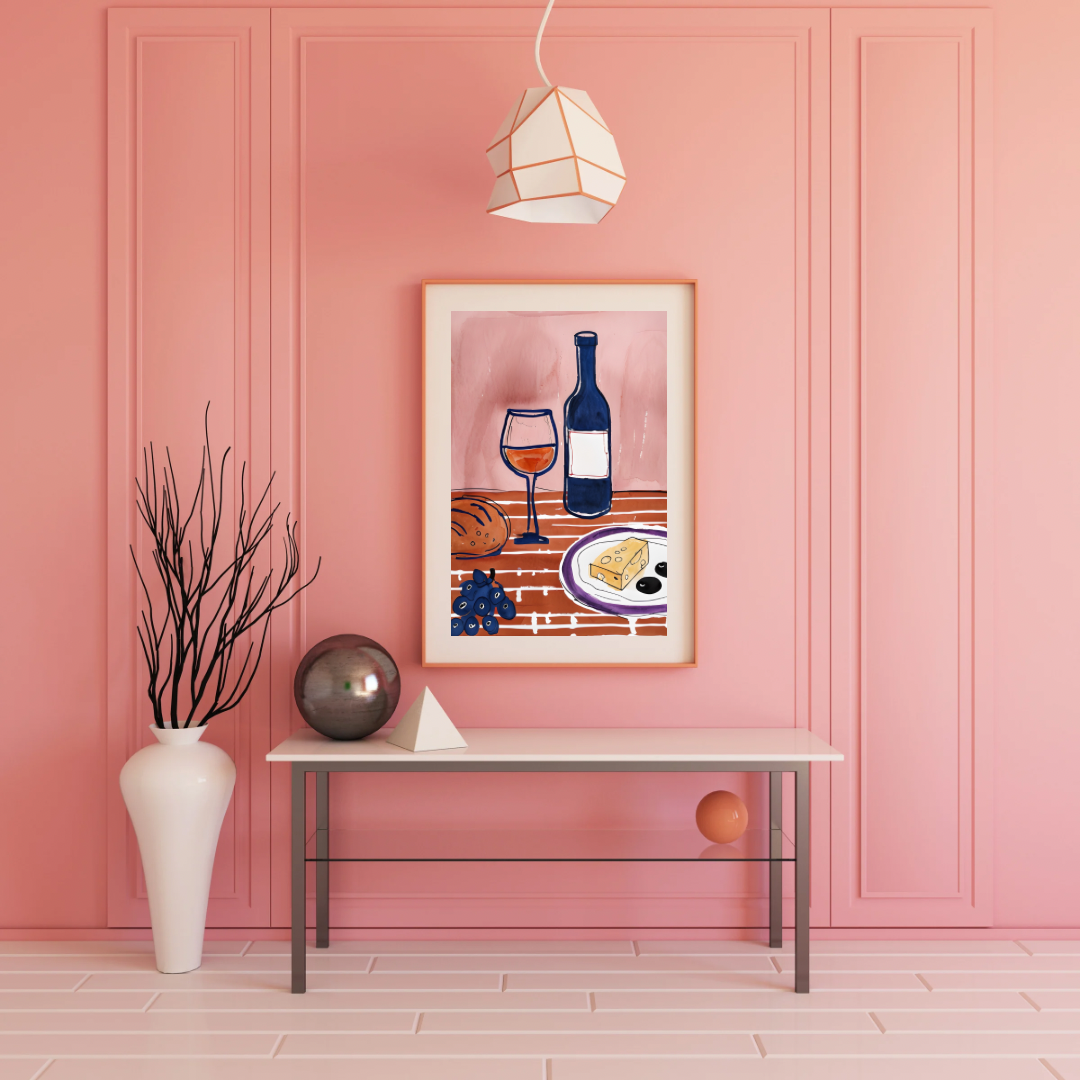Framed wine and cheese artwork on a pink wall with a table and decorative items.